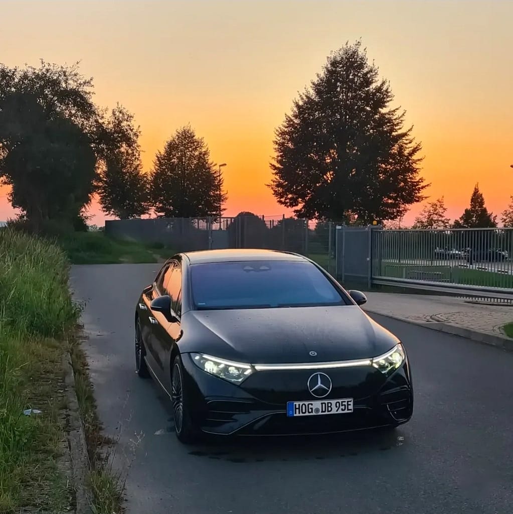 Mercedes-Benz EQS in Schwarz in Frontansicht bei Sonnenuntergang mit eingeschalteter LED-Lichtsignatur auf einer Straße fotografiert
