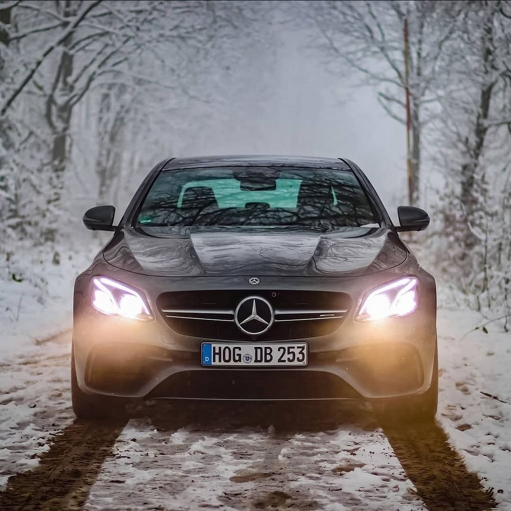 Mercedes-AMG E63 in Frontansicht auf verschneitem Waldweg mit eingeschalteten LED-Scheinwerfern fotografiert