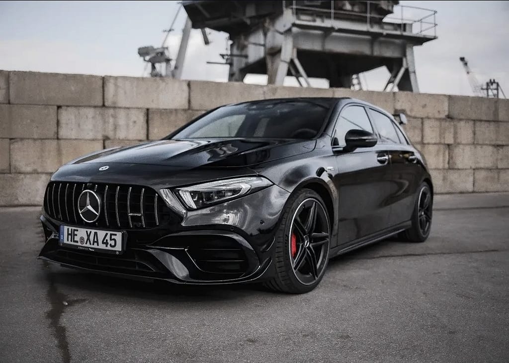 Schwarzer Mercedes-AMG A 45 S (W177) vor industrieller Hafenkulisse mit markantem Panamericana-Grill, roten Bremssätteln und sportlichem Aerodynamikpaket. Hochwertige Automotive Fotografie mit Fokus auf Performance und Design.