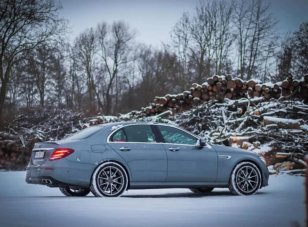 Mercedes-AMG E63 in Grau in Seitenansicht auf verschneiter Fläche mit beleuchteten Rückleuchten fotografiert