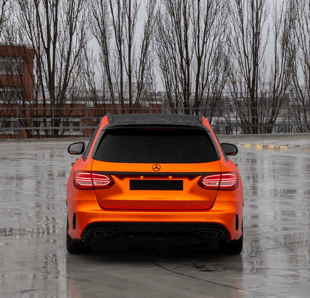 Orange foliertes Mercedes-Benz C 43 AMG T-Modell (S205) auf einem regennassen Parkdeck mit Spiegelungen auf dem Asphalt, schwarzem Dach und sportlichen AMG-Designelementen.