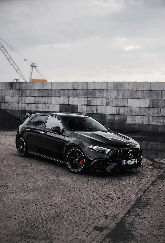 Schwarzer Mercedes-AMG A 45 S (W177) vor industrieller Hafenkulisse mit markantem Panamericana-Grill, roten Bremssätteln und sportlichem Aerodynamikpaket. Hochwertige Automotive Fotografie mit Fokus auf Performance und Design.