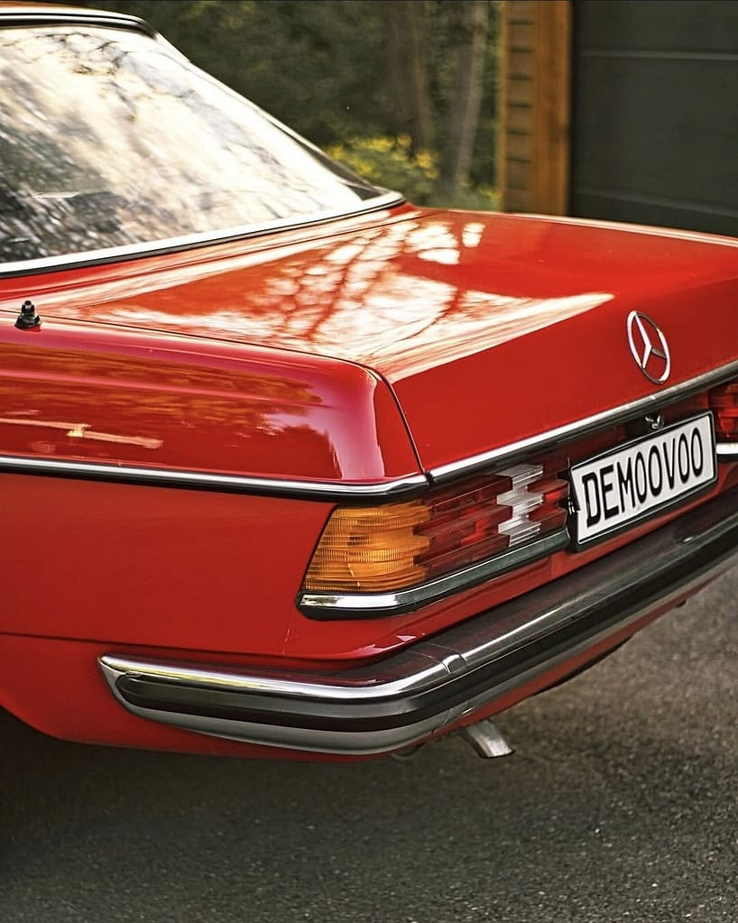 Mercedes-Benz C123 Coupé in roter Lackierung bei Abendlicht vor einer Garage fotografiert. Klassischer Mercedes-Benz Oldtimer mit Chromgrill und zeitlosem Coupé-Design.