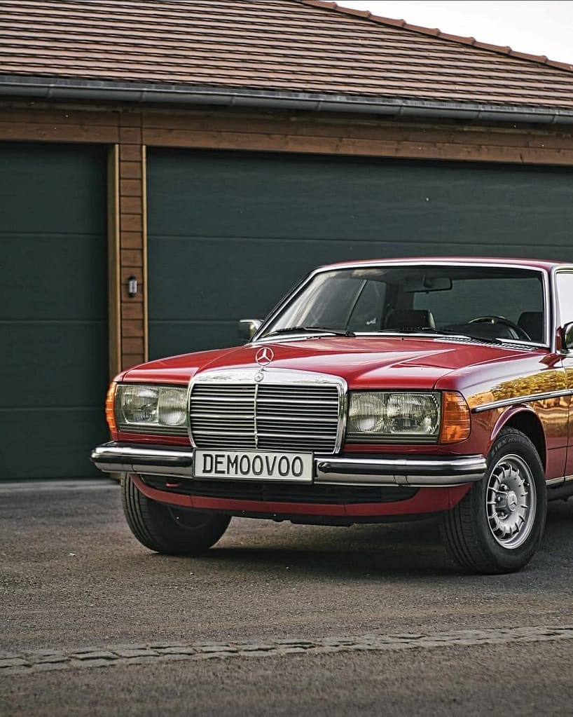 Mercedes-Benz C123 Coupé in roter Lackierung bei Abendlicht vor einer Garage fotografiert. Klassischer Mercedes-Benz Oldtimer mit Chromgrill und zeitlosem Coupé-Design.