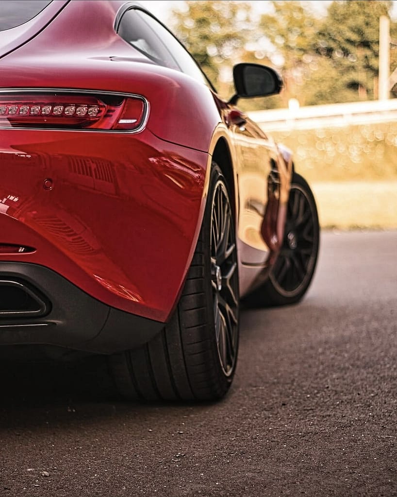Detailaufnahmen eines roten Mercedes-AMG GT S (C190) mit Panamericana-Grill, LED-Heckleuchten, AMG-Felgen und V8-Biturbo-Details vor einer historischen Industriekulisse.