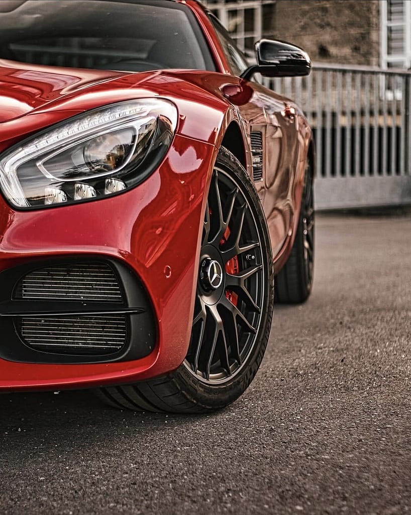 Detailaufnahmen eines roten Mercedes-AMG GT S (C190) mit Panamericana-Grill, LED-Heckleuchten, AMG-Felgen und V8-Biturbo-Details vor einer historischen Industriekulisse.