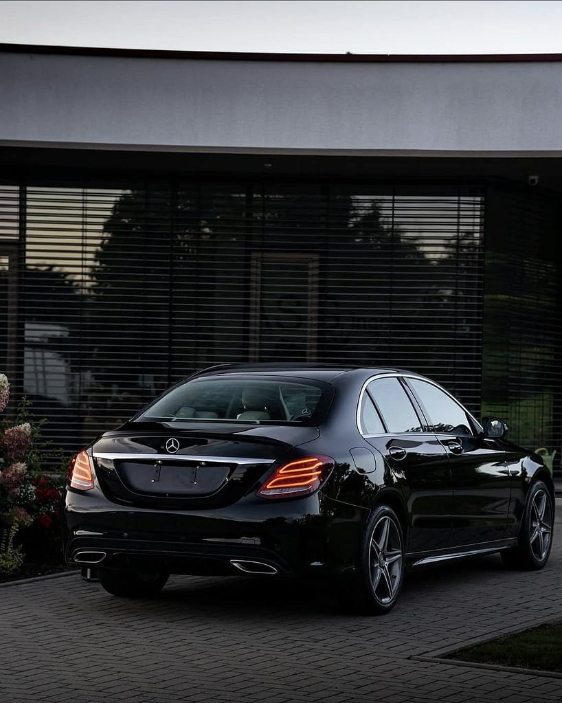 Mercedes-Benz C-Klasse Limousine (W205) in Schwarz während eines Fotoshootings bei Abenddämmerung mit Front-, Heck- und Detailaufnahmen vor moderner Architektur.