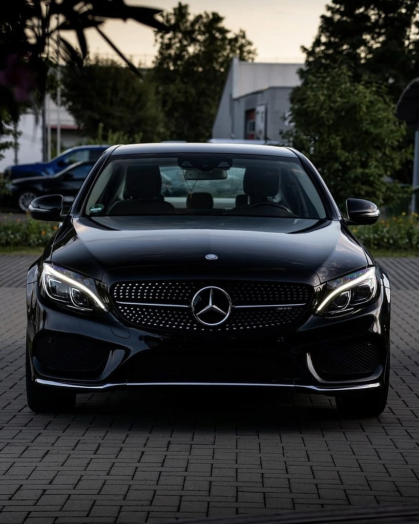 Mercedes-Benz C-Klasse Limousine (W205) in Schwarz während eines Fotoshootings bei Abenddämmerung mit Front-, Heck- und Detailaufnahmen vor moderner Architektur.