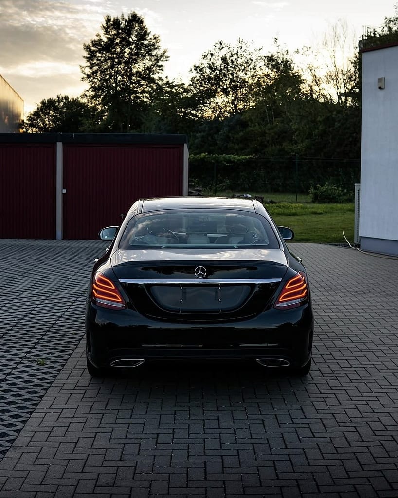 Mercedes-Benz C-Klasse Limousine (W205) in Schwarz während eines Fotoshootings bei Abenddämmerung mit Front-, Heck- und Detailaufnahmen vor moderner Architektur.