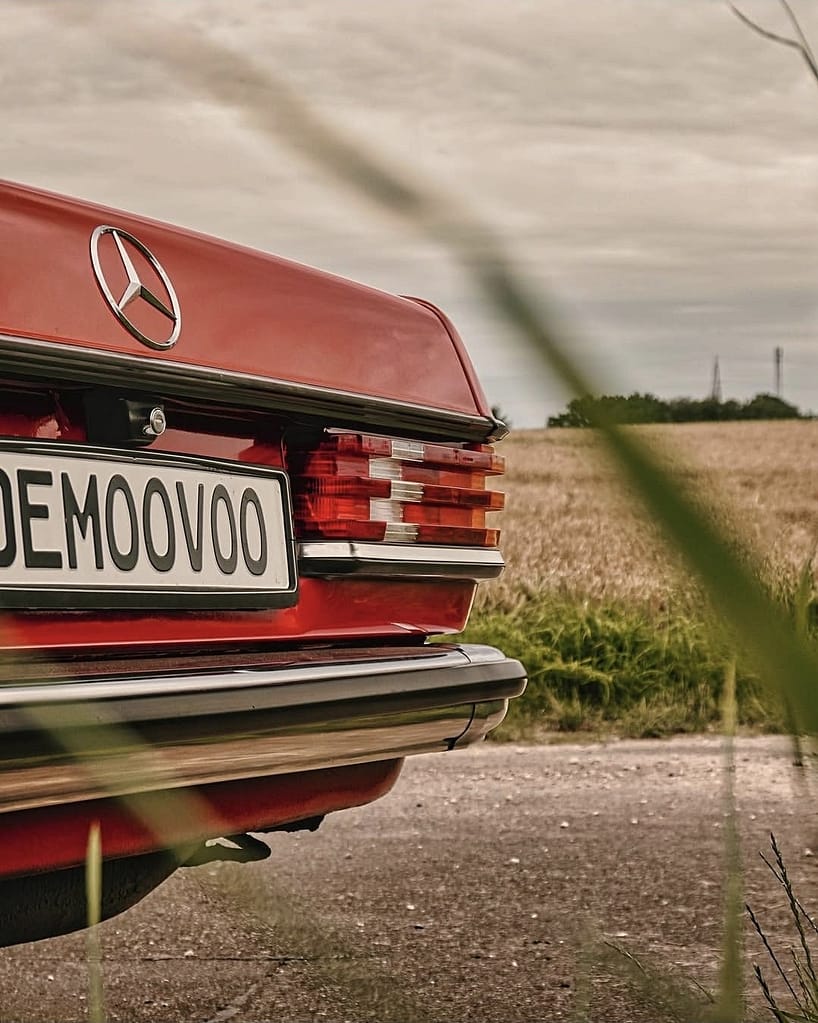 Mercedes-Benz C123 Coupé in klassischem Rot auf einer ländlichen Straße vor Getreidefeldern und dramatischem Wolkenhimmel – hochwertige Automotive Photography von MB DOME.