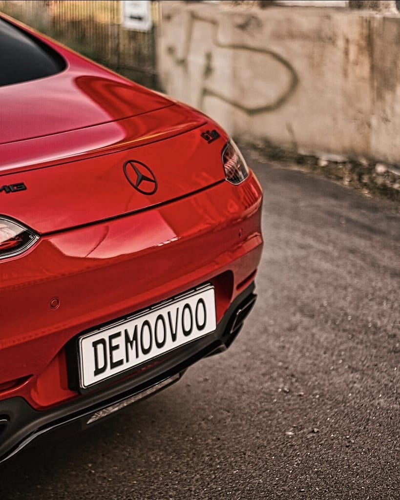 Detailaufnahmen eines roten Mercedes-AMG GT S (C190) mit Panamericana-Grill, LED-Heckleuchten, AMG-Felgen und V8-Biturbo-Details vor einer historischen Industriekulisse.