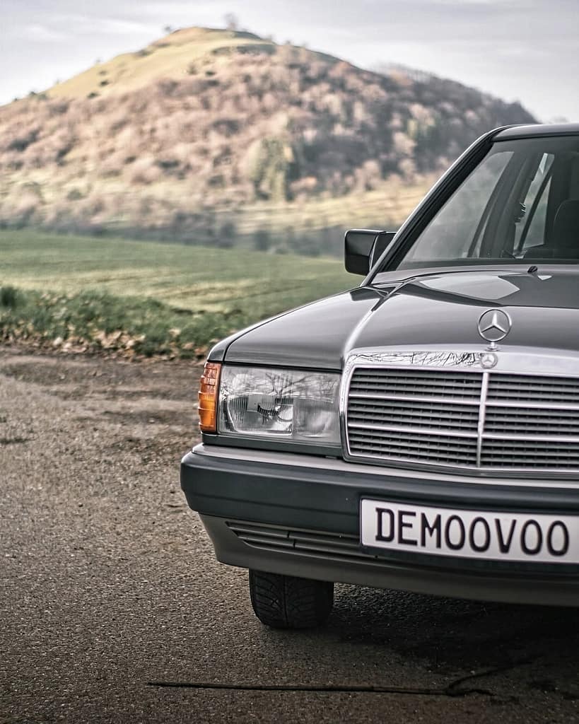 Mercedes-Benz 190 E (W201) in grauer Lackierung vor einer malerischen Hügellandschaft – klassischer Mercedes-Youngtimer mit zeitlosem Design und eleganter Linienführung.