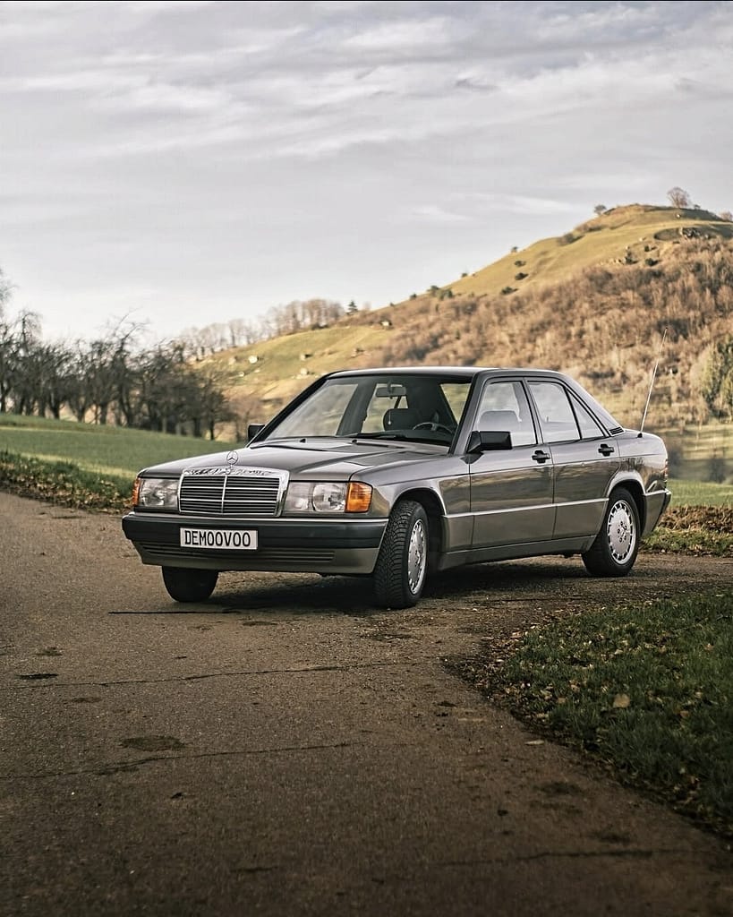 Mercedes-Benz 190 E (W201) in grauer Lackierung vor einer malerischen Hügellandschaft – klassischer Mercedes-Youngtimer mit zeitlosem Design und eleganter Linienführung.
