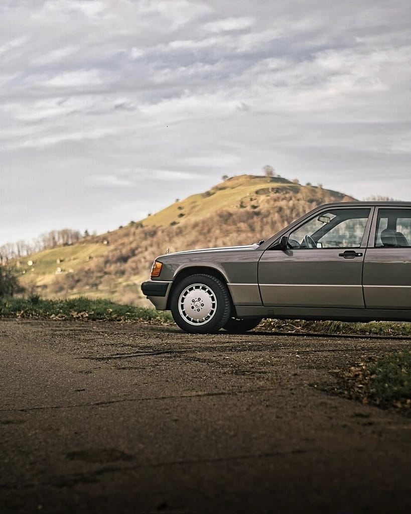 Mercedes-Benz 190 E (W201) in grauer Lackierung vor einer malerischen Hügellandschaft – klassischer Mercedes-Youngtimer mit zeitlosem Design und eleganter Linienführung.