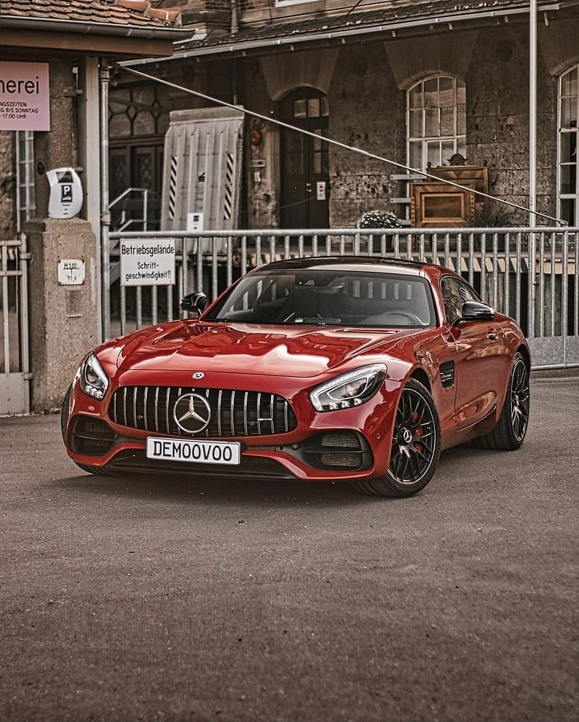 Detailaufnahmen eines roten Mercedes-AMG GT S (C190) mit Panamericana-Grill, LED-Heckleuchten, AMG-Felgen und V8-Biturbo-Details vor einer historischen Industriekulisse.