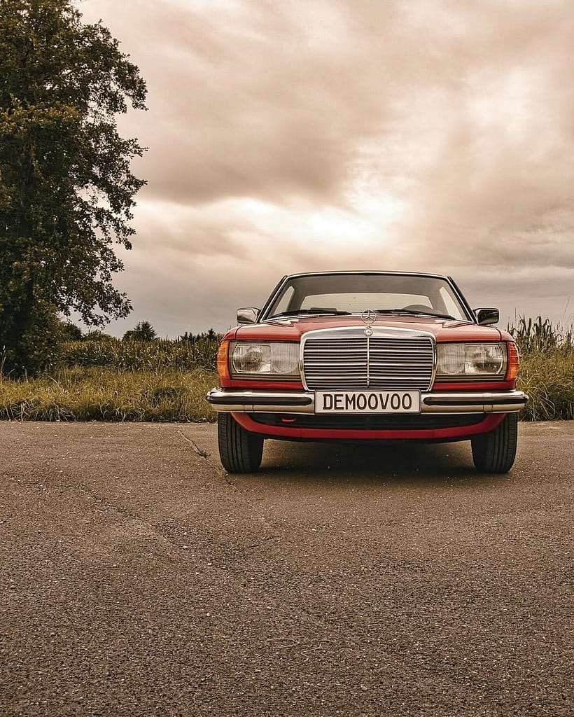 Mercedes-Benz C123 Coupé in klassischem Rot auf einer ländlichen Straße vor Getreidefeldern und dramatischem Wolkenhimmel – hochwertige Automotive Photography von MB DOME.