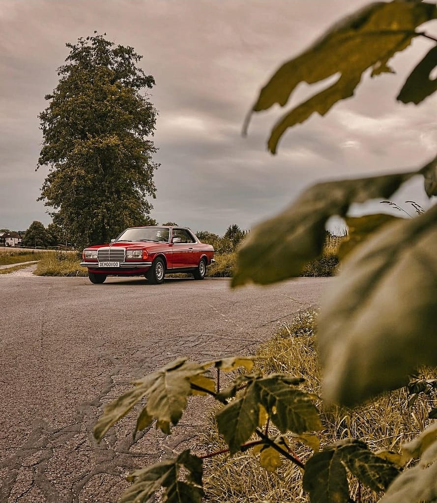 Mercedes-Benz C123 Coupé in klassischem Rot auf einer Landstraße mit Chromgrill und zeitlosem Design – hochwertige Automotive Photography von MB-DOME.
