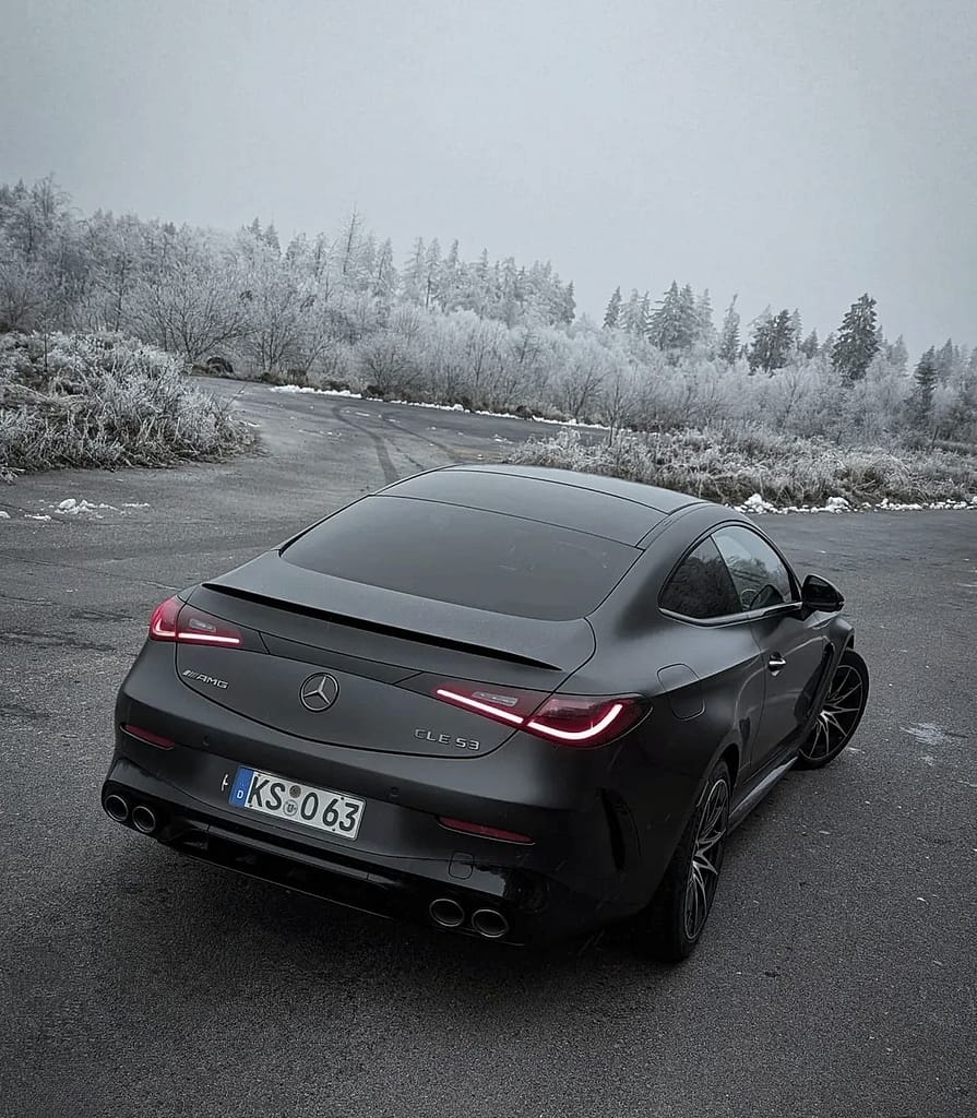 Mercedes-AMG CLE 53 4MATIC+ Coupé in mattschwarz auf winterlicher Straße mit vereister Waldlandschaft im Hintergrund, aufgenommen bei kaltem Winterwetter.