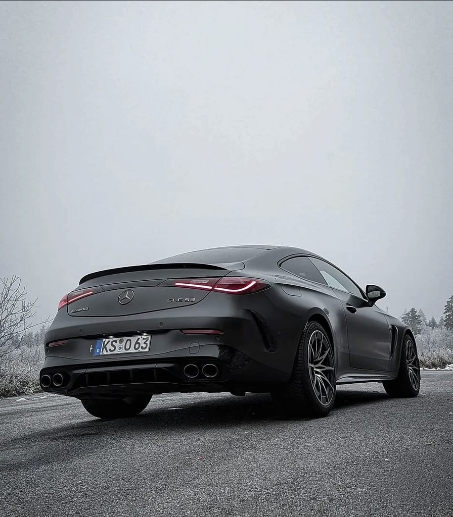 Mercedes-AMG CLE 53 4MATIC+ Coupé in mattschwarz auf winterlicher Straße mit vereister Waldlandschaft im Hintergrund, aufgenommen bei kaltem Winterwetter.