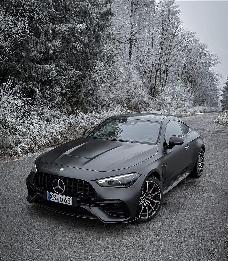 Mercedes-AMG CLE 53 4MATIC+ Coupé in mattschwarz auf winterlicher Straße mit vereister Waldlandschaft im Hintergrund, aufgenommen bei kaltem Winterwetter.
