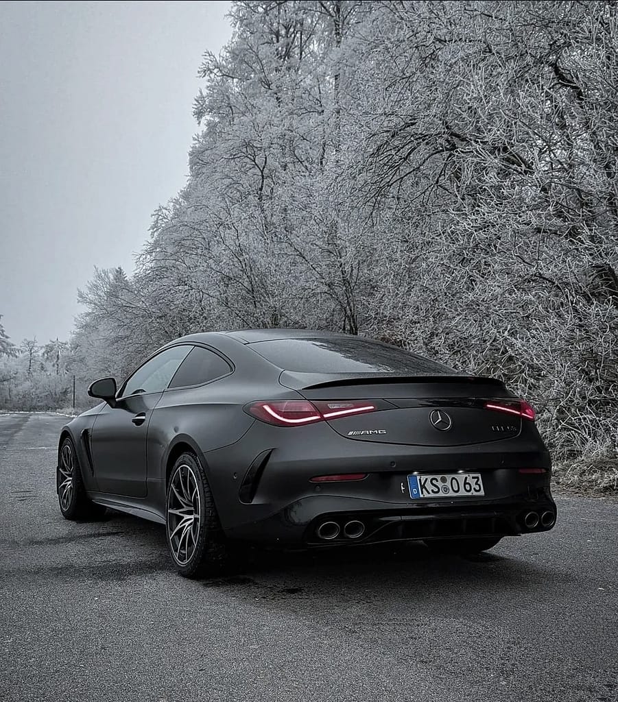 Mercedes-AMG CLE 53 4MATIC+ Coupé in mattschwarz auf winterlicher Straße mit vereister Waldlandschaft im Hintergrund, aufgenommen bei kaltem Winterwetter.