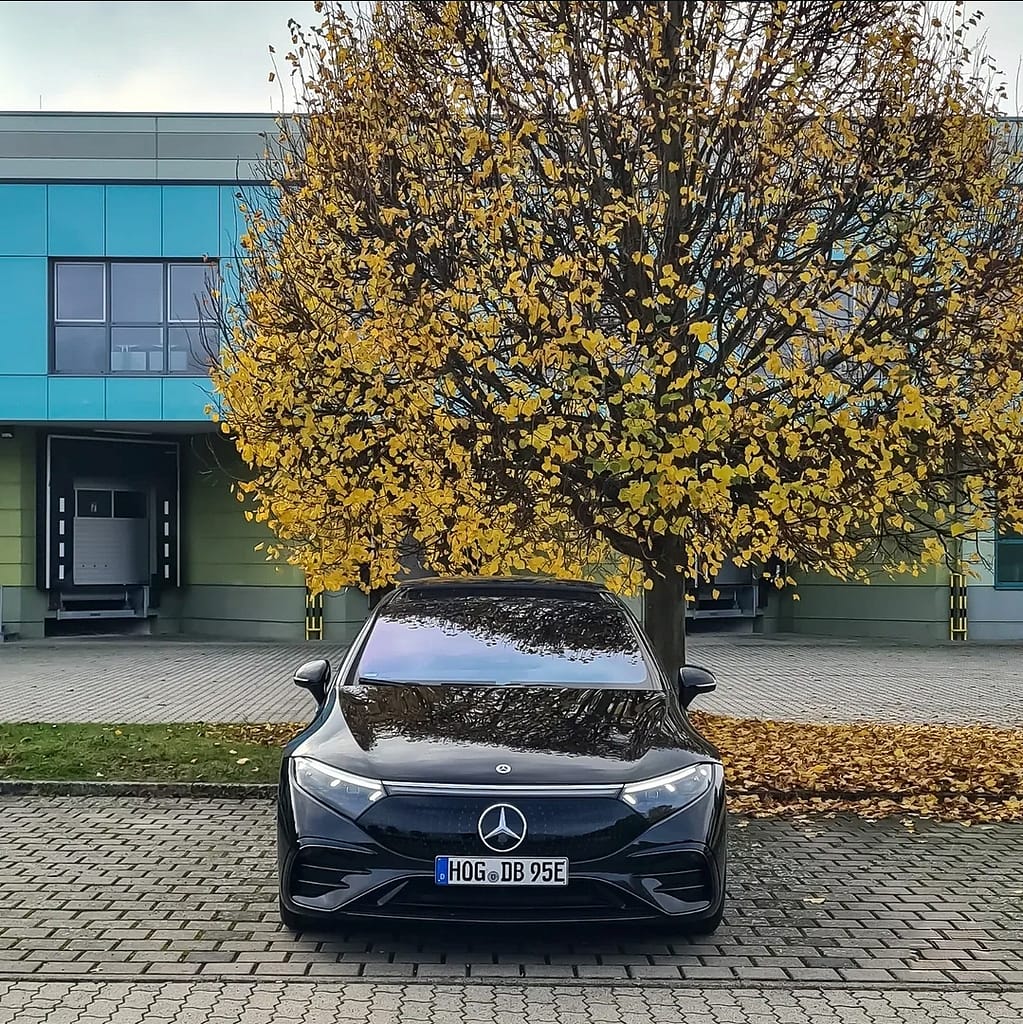 Mercedes-Benz EQS in Schwarz frontal vor gelbem Herbstbaum mit futuristischem Elektroauto Design