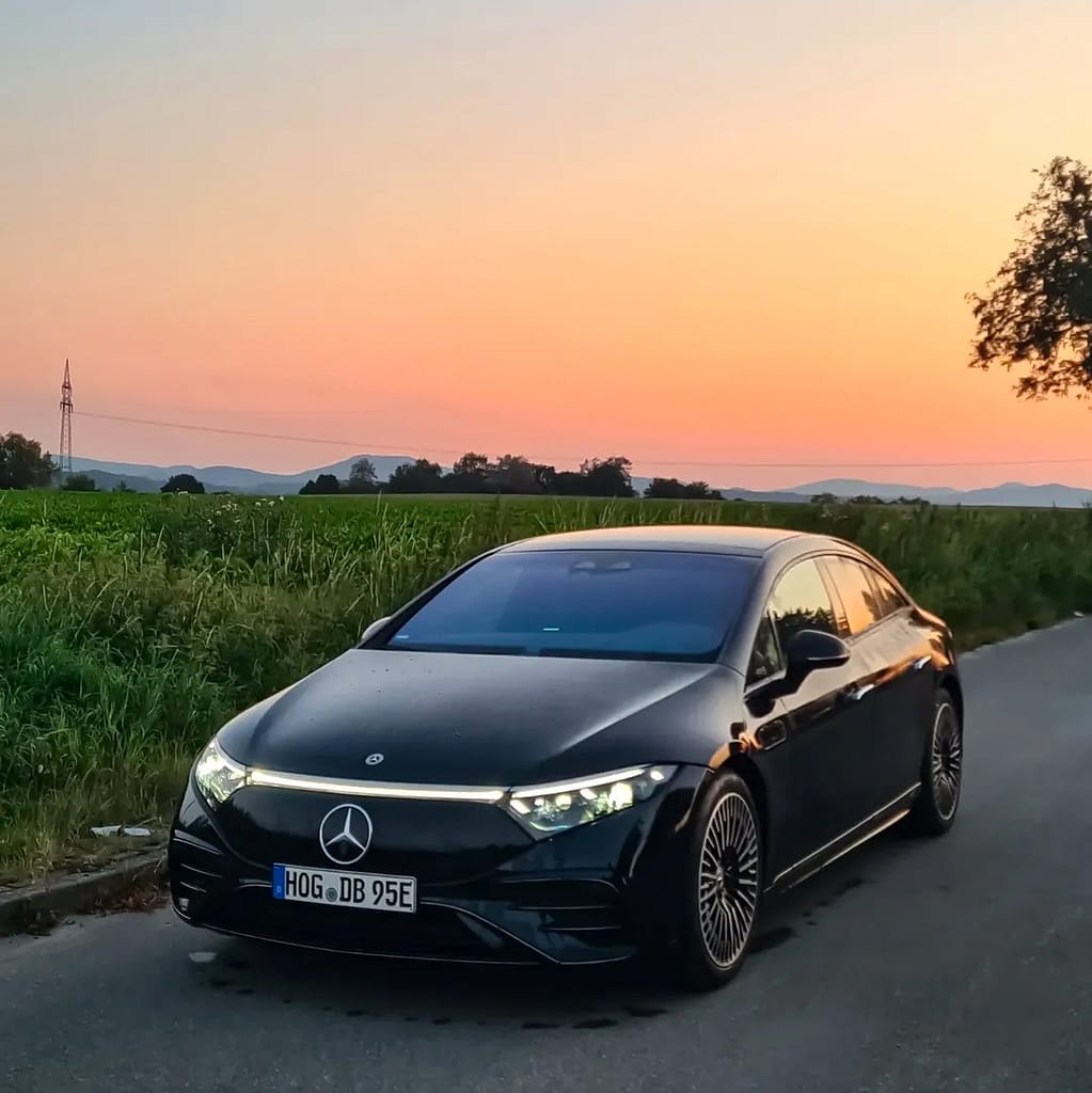 Mercedes-Benz EQS in Schwarz bei Sonnenuntergang auf einer Landstraße mit eingeschalteter LED-Lichtsignatur fotografiert