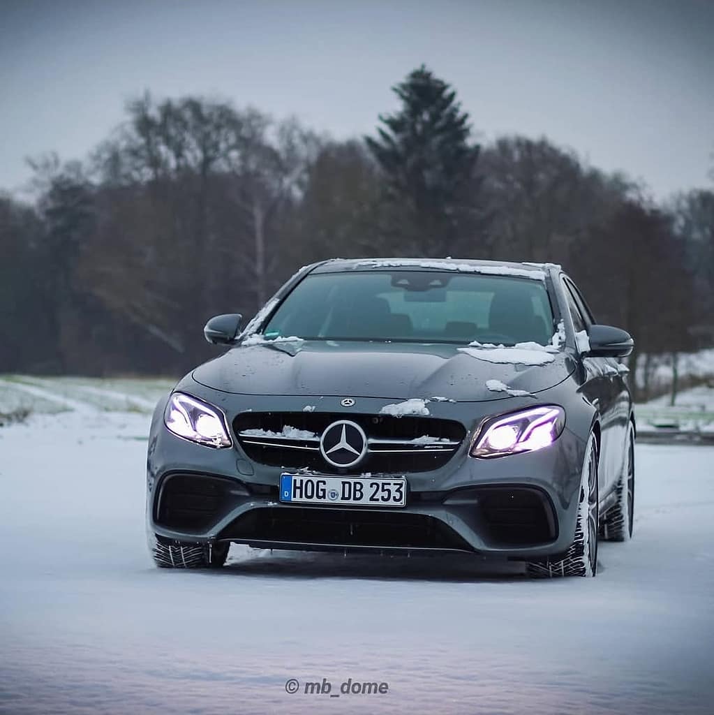Mercedes-AMG E63 in Grau in Frontansicht auf verschneiter Straße mit eingeschalteten LED-Scheinwerfern fotografiert