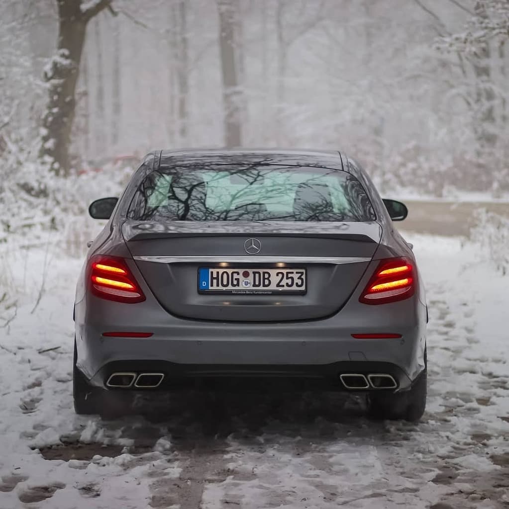 Mercedes-AMG E63 in Heckansicht auf verschneitem Waldweg mit eingeschalteten LED-Rückleuchten fotografiert
