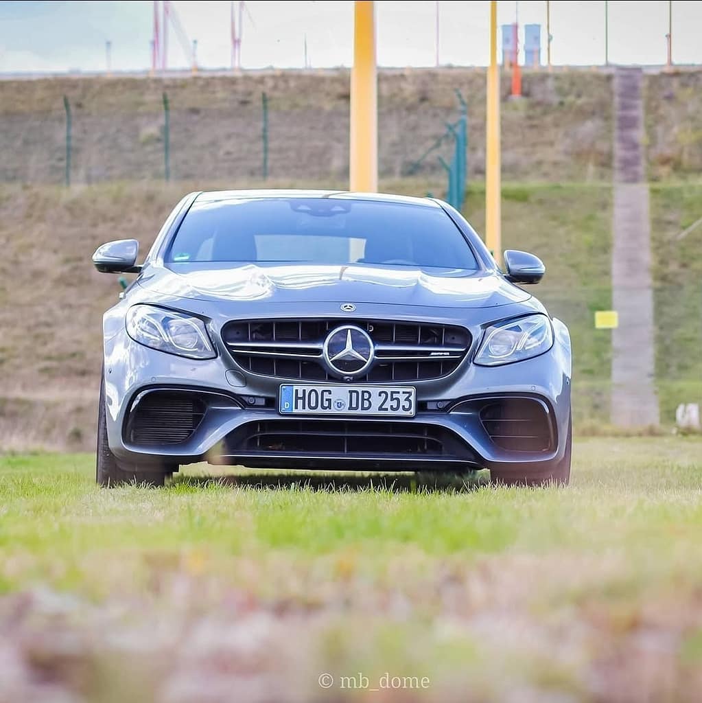 Mercedes-AMG E63 in symmetrischer Frontansicht auf einer Wiese mit offener Landschaft im Hintergrund fotografiert