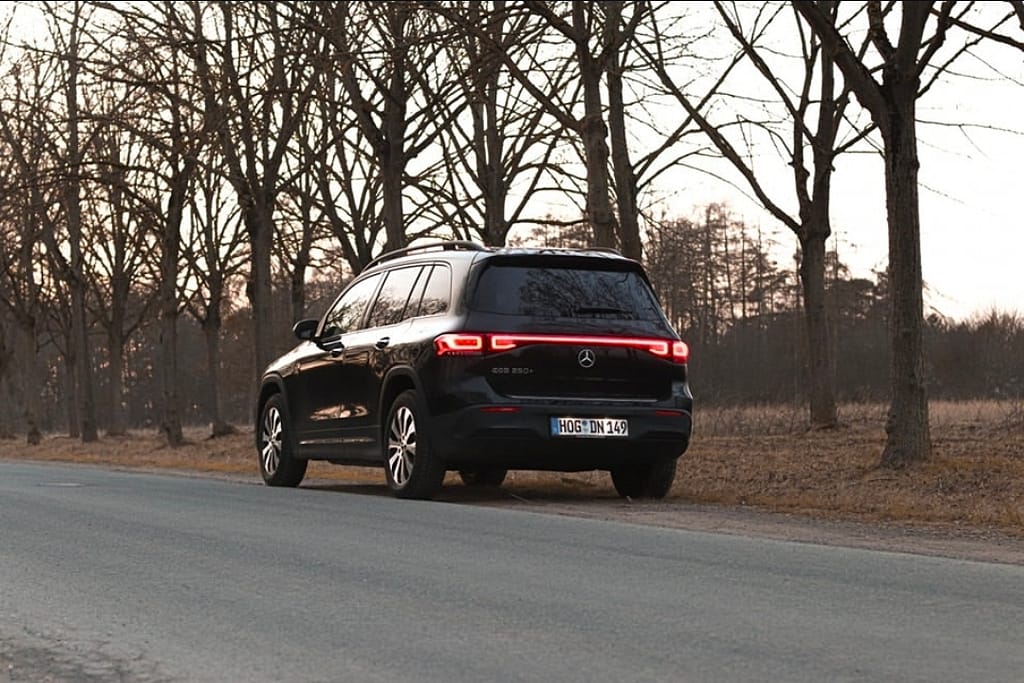 Mercedes-Benz EQB in Schwarz in Heckansicht am Straßenrand bei Sonnenuntergang mit durchgehendem LED-Rücklichtband fotografiert