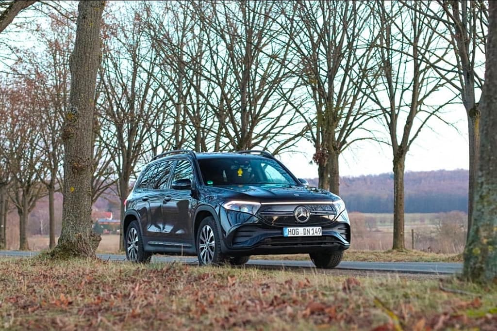 Mercedes-Benz EQB in Schwarz in Frontansicht auf einer Landstraße zwischen Bäumen bei Tageslicht fotografiert