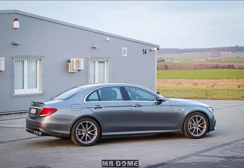 Mercedes-AMG E63 in Seitenansicht vor einem modernen Industriegebäude mit Feldern im Hintergrund fotografiert