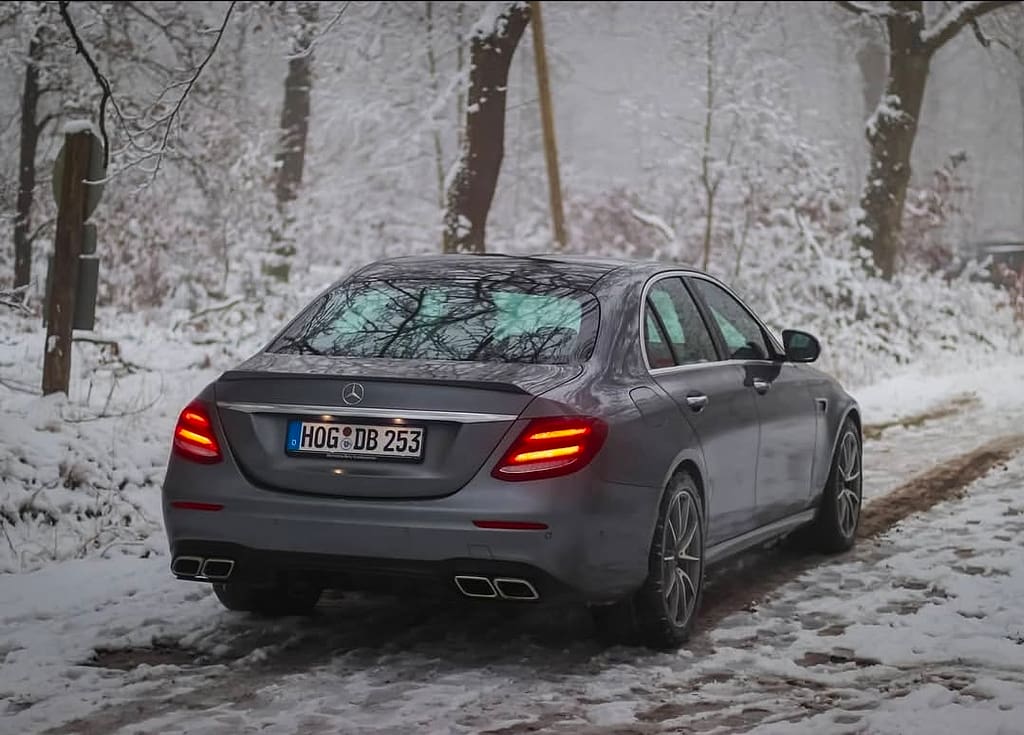 Mercedes-AMG E63 in Heck-Seitenansicht auf verschneitem Waldweg mit eingeschalteten LED-Rückleuchten fotografiert
