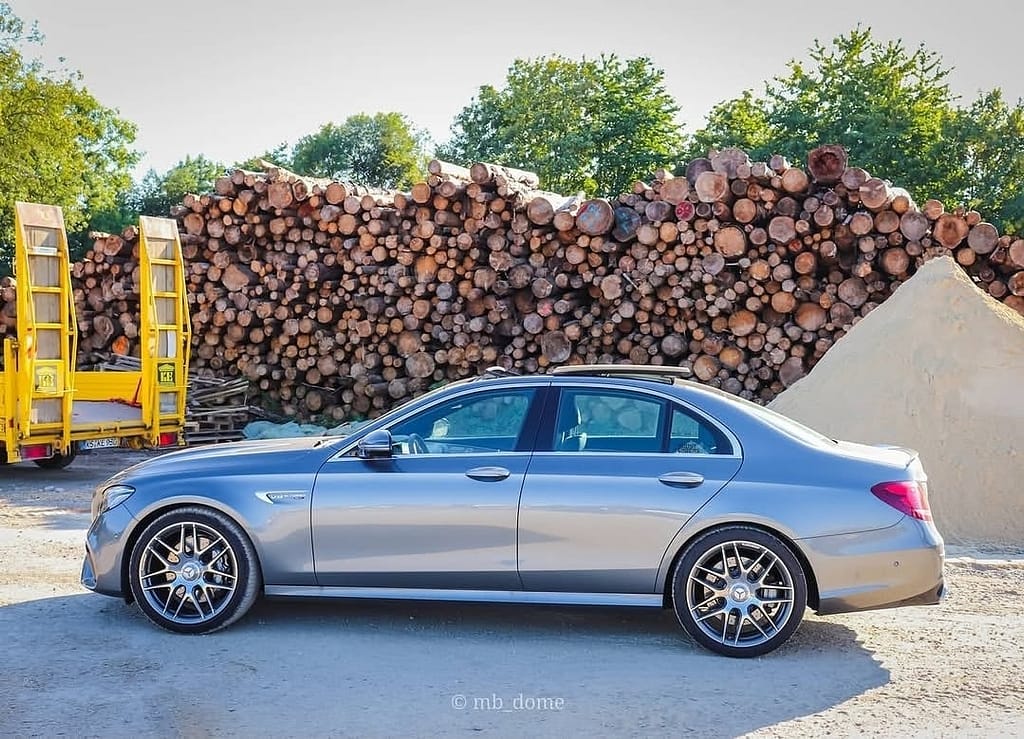Mercedes-AMG E63 in Grau in Seitenansicht auf einem Industriegelände mit Holzstapeln im Hintergrund fotografiert