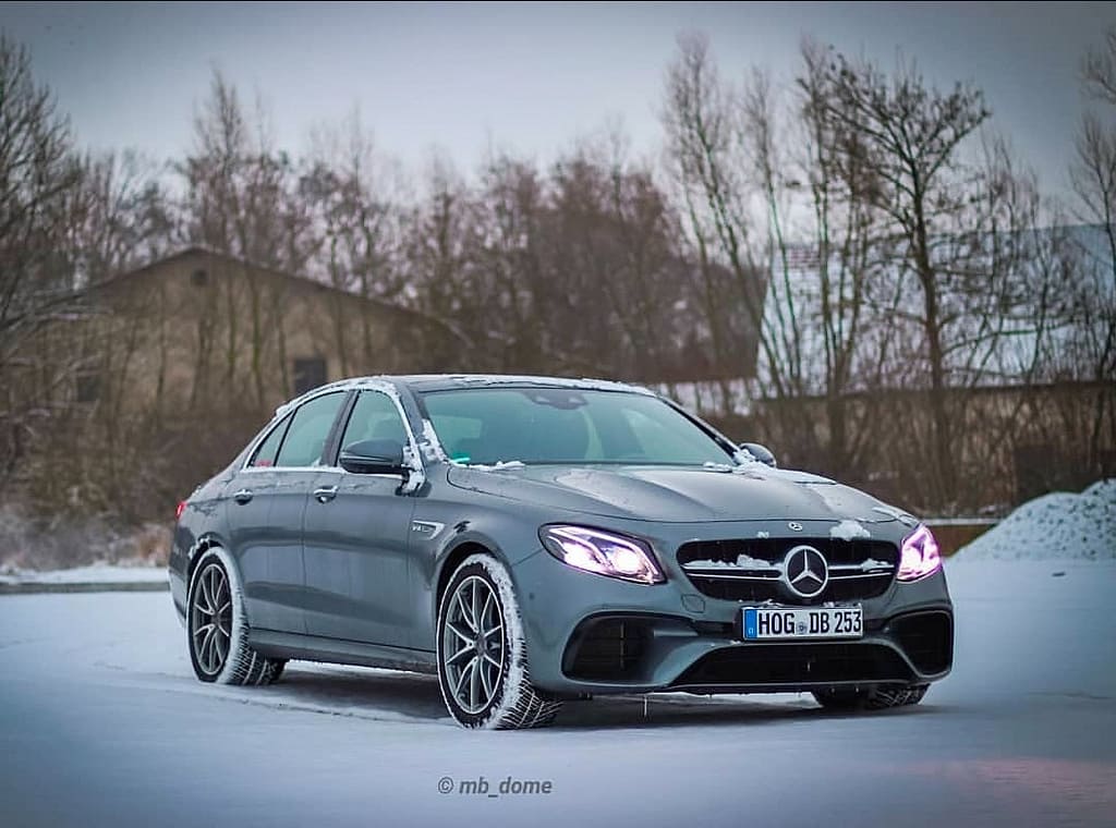 Mercedes-AMG E63 in Grau in Front-Seitenansicht auf verschneiter Straße mit eingeschalteten LED-Scheinwerfern fotografiert
