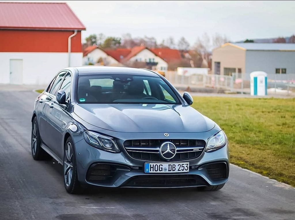 Mercedes-AMG E63 in Frontansicht auf einer ruhigen Straße mit moderner Architektur im Hintergrund und klarer Sicht auf die charakteristische AMG-Front.