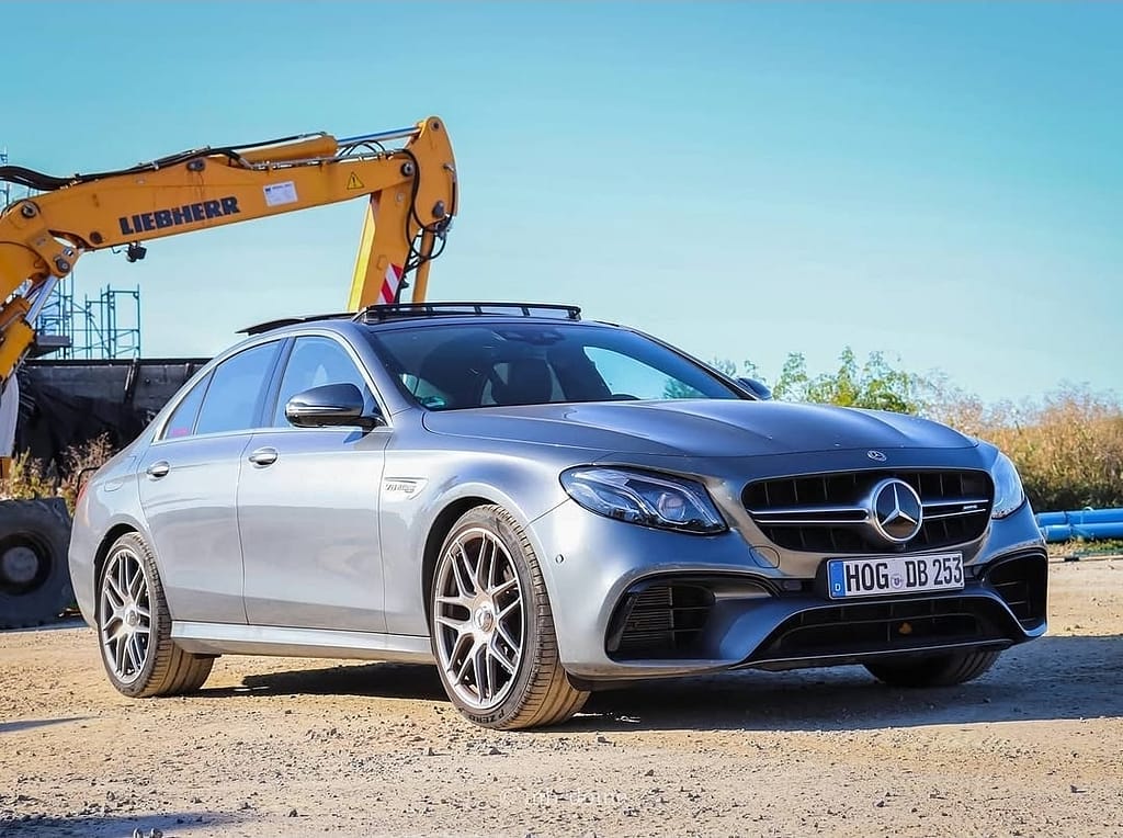 Mercedes-AMG E63 in Silber in Front-Seitenansicht auf einem Industriegelände mit Bagger im Hintergrund fotografiert