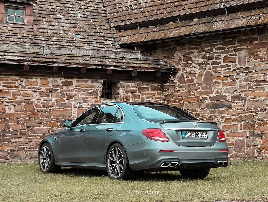 Mercedes-AMG E63 in Heck-Seitenansicht vor einer historischen Natursteinmauer und alten Ziegeldächern fotografiert