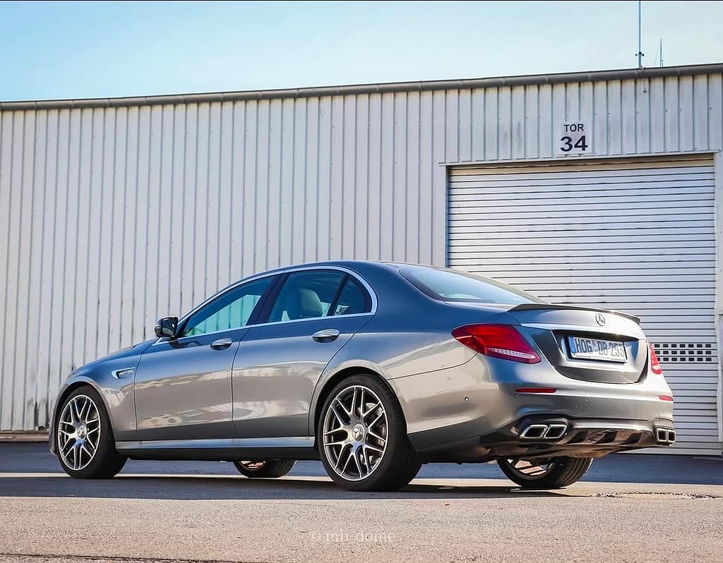 Mercedes-AMG E63 in Heck-Seitenansicht vor einer weißen Industriehalle mit Rolltor, sportliche AMG-Limousine mit markanter Heckpartie und vier Endrohren.