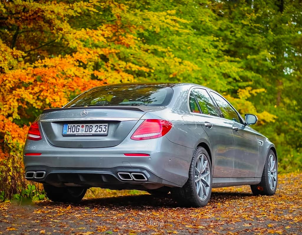 Mercedes-AMG E63 in Heck-Seitenansicht auf einer herbstlichen Waldstraße mit buntem Laub und gelb-orangefarbenen Bäumen im Hintergrund