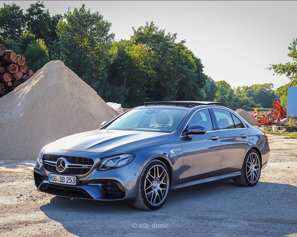 Mercedes-AMG E63 in Grau in Front-Seitenansicht auf einem Industriegelände mit Sandhügeln im Hintergrund fotografiert