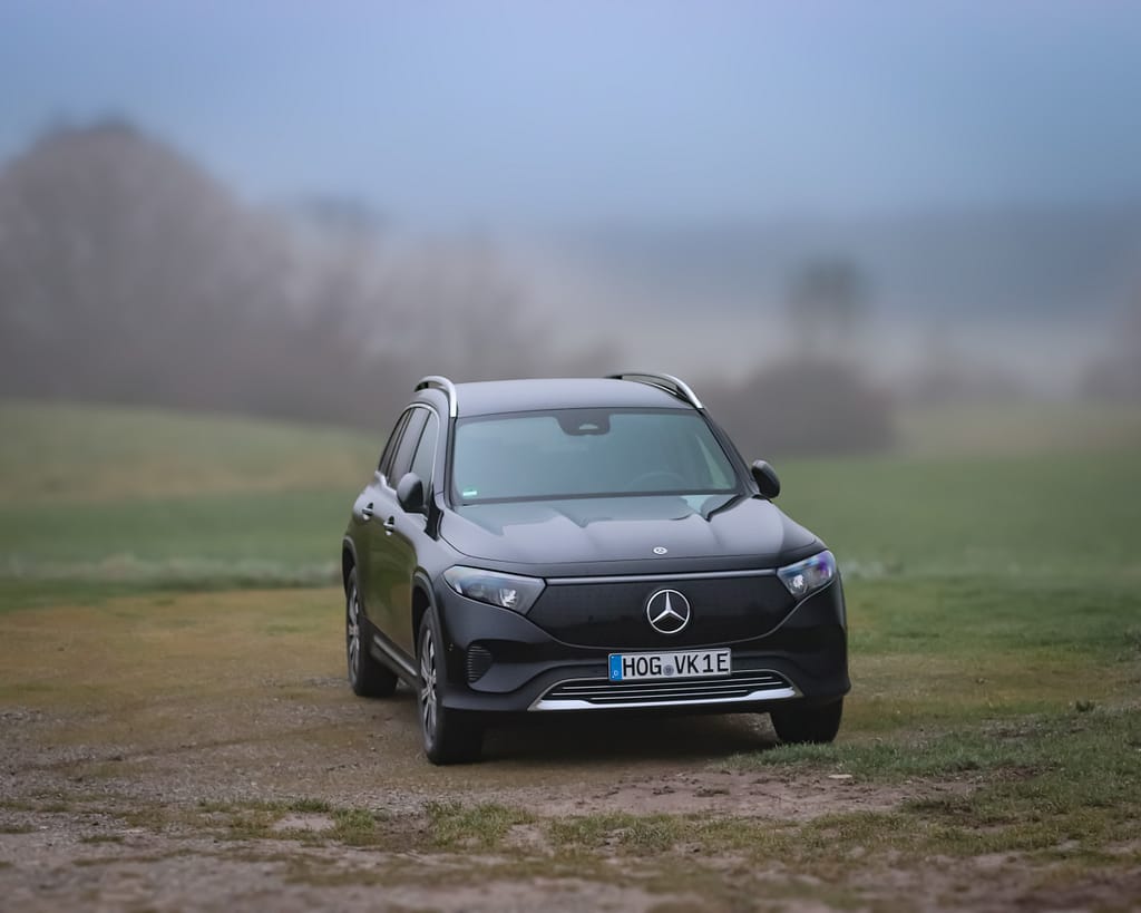 Mercedes-Benz EQB Elektro SUV in schwarzer Lackierung auf unbefestigtem Weg in nebliger Landschaft mit Front-, Seiten- und Heckansicht