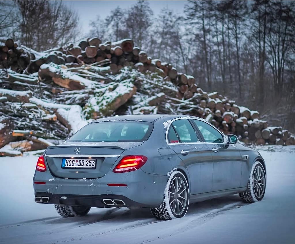 Mercedes-AMG E63 in Grau in Heck-Seitenansicht auf verschneiter Straße mit eingeschalteten LED-Rückleuchten fotografiert