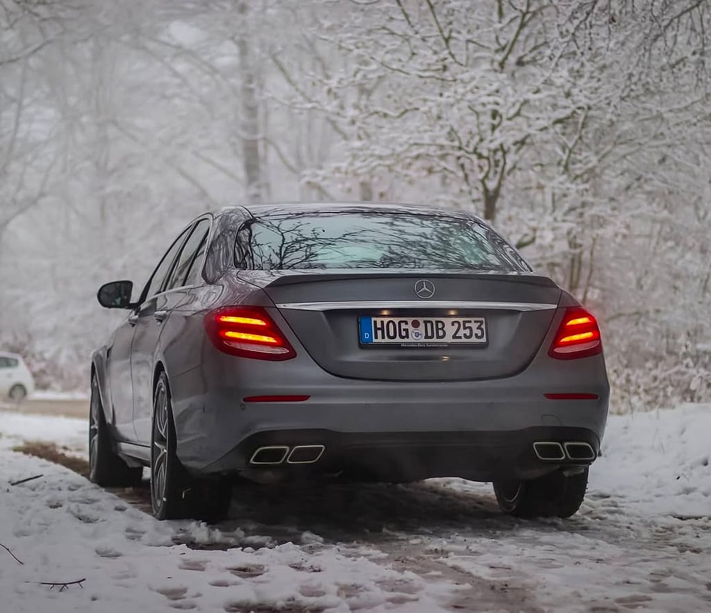 Mercedes-AMG E63 in Heckansicht auf verschneitem Waldweg mit leuchtenden LED-Rückleuchten fotografiert