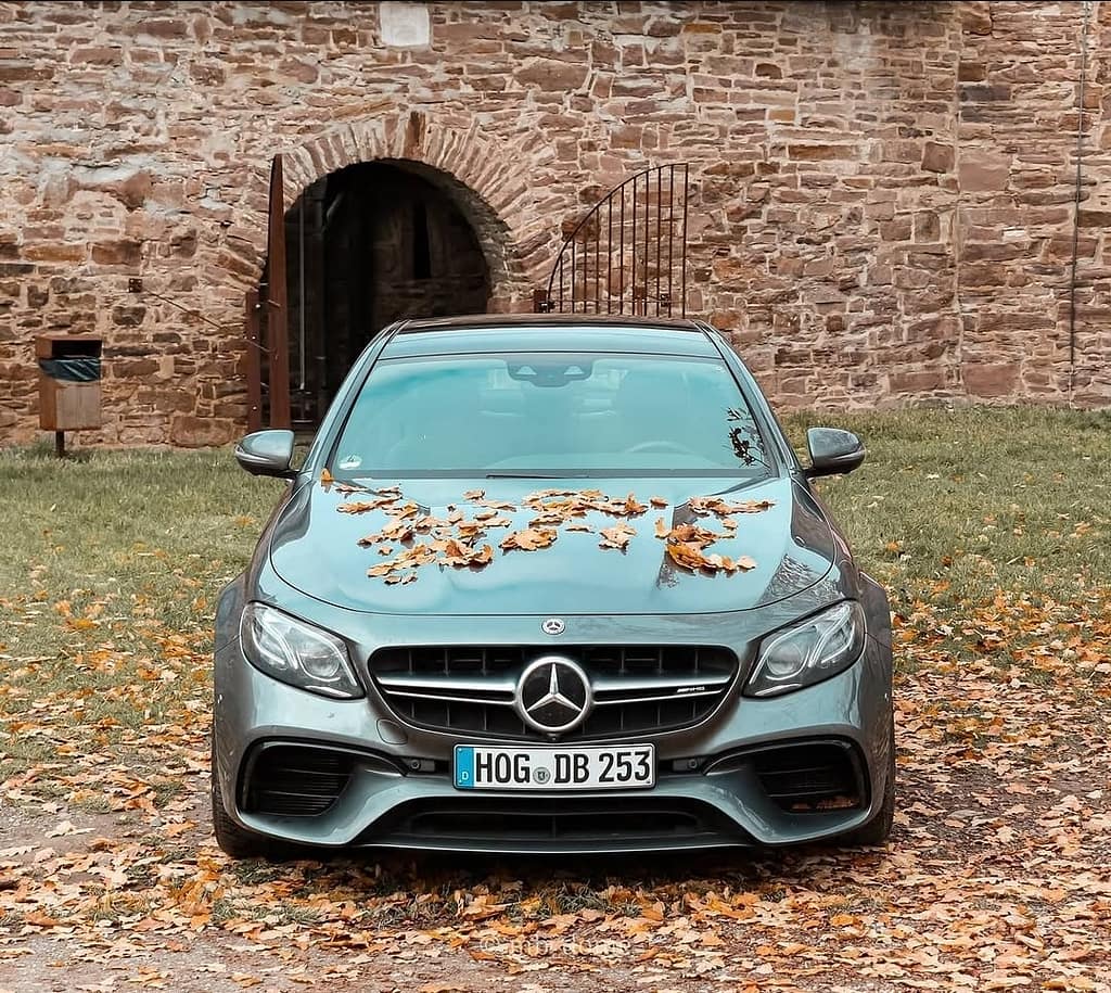 Mercedes-AMG E63 in Frontansicht mit Herbstlaub auf der Motorhaube vor einer historischen Natursteinmauer mit Torbogen