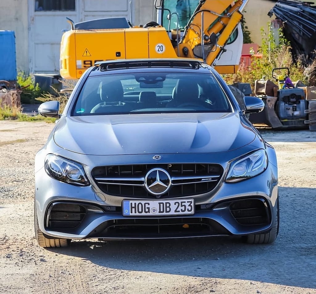 Mercedes-AMG E63 in Grau in symmetrischer Frontansicht auf einem Industriegelände mit Bagger im Hintergrund fotografiert