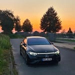 Mercedes-Benz EQS in Schwarz in Frontansicht bei Sonnenuntergang mit eingeschalteter LED-Lichtsignatur auf einer Straße fotografiert