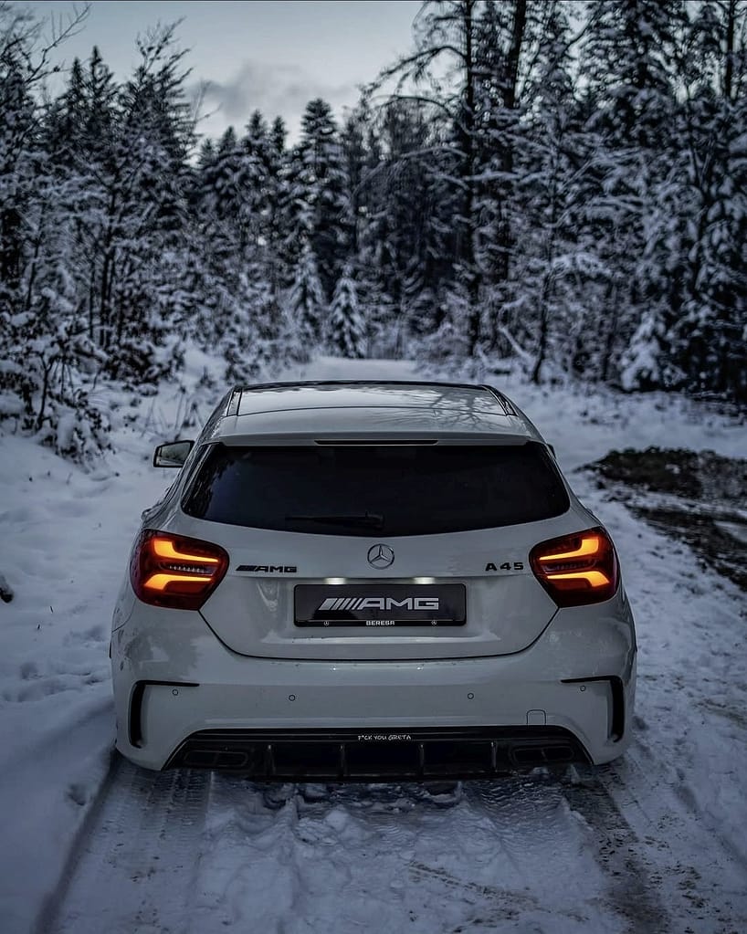 Heckansicht eines weißen Mercedes-AMG A45 W176 auf verschneiter Waldstraße mit leuchtenden Rücklichtern