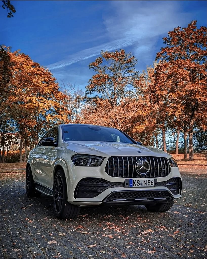Weißer Mercedes-AMG GLE 53 Coupé C167 mit Panamericana Grill und schwarzem AMG Exterieur im Herbstpark mit bunten Bäumen